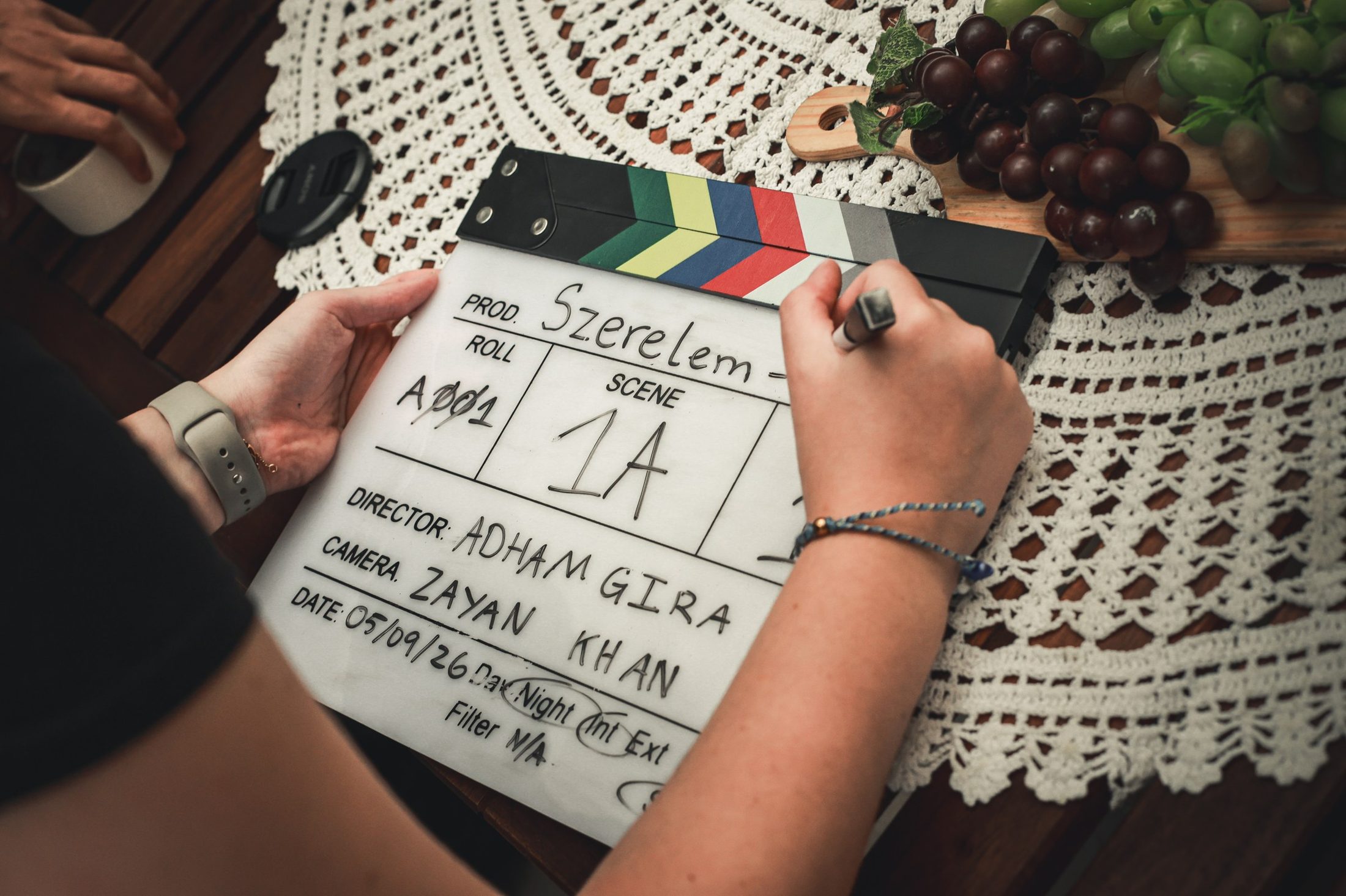 A hand writes on the Szerelem clapperboard on a lace tablecloth
